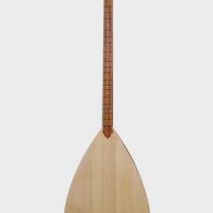 May include: A light-colored, pear-shaped stringed instrument, likely a saz or similar folk instrument. It features a long neck with frets, tuning pegs at the head, and a sound hole. The body is made of wood, with a natural finish.