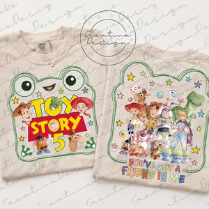 May include: Two beige t-shirts featuring Toy Story graphics. The left shirt displays a frog outline, the text "TOY STORY 5," and various characters. The right shirt shows a group of animated characters and the text "YOU'VE GOT A FRIEND IN ME."
