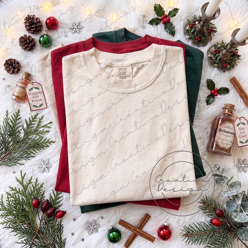 K&ouml;nnte beinhalten: Ein Stapel aus drei T-Shirts mit Rundhalsausschnitt in Creme, Dunkelrot und Dunkelgr&uuml;n. Das oberste cremefarbene T-Shirt hat ein Comfort Colors-Etikett am inneren Halsausschnitt. Die T-Shirts sind in einem geschichteten Stapel angeordnet.