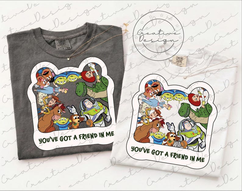 May include: A charcoal grey t-shirt and a white t-shirt, each featuring a graphic print of various animated characters from Toy Story arranged in a circle, with the text YOU'VE GOT A FRIEND IN ME printed in black below the character illustration.