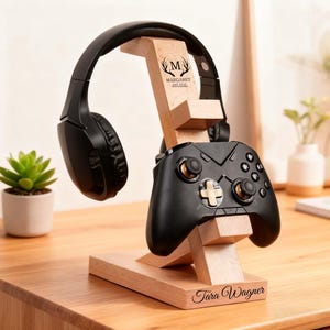 May include: A wooden stand for headphones and a game controller. The stand is made of light-coloured wood and holds a black headset and game controller. The stand is engraved with the names "Margaret" and "Tara Wagner".