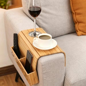 Pode incluir: Uma caneca de cerâmica branca com uma alça preta e o texto "But First, Coffee" em preto, em negrito. A caneca está sobre uma superfície branca.