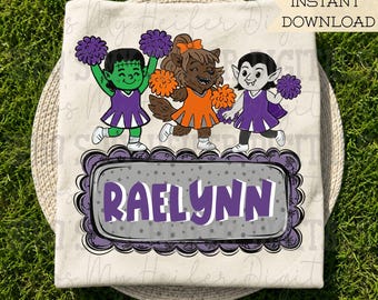 May include: A cream-colored t-shirt featuring a graphic of three monster cheerleaders in purple and orange uniforms with pom-poms. Below them is a gray rectangular frame with a scalloped purple border containing the name RAELYNN in purple text.
