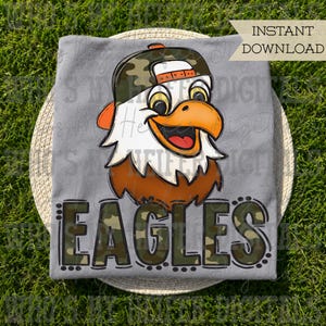 Könnte beinhalten: Ein graues T-Shirt mit einem Cartoon-Adlerkopf, der eine Camouflage-Baseballkappe trägt, und dem Wort EAGLES darunter in einem passenden Camouflage-Muster. Der Text INSTANT DOWNLOAD ist in der oberen rechten Ecke des Bildes zu sehen.