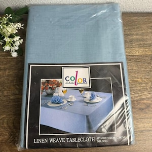 May include: A light blue linen weave tablecloth packaged in clear plastic. The label features the text Color Classics and Linen Weave Tablecloth, with a photo of a table setting. The dimensions are listed as 60 inches by 102 inches.