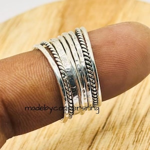 May include: A stackable silver ring set with various textures, including hammered and rope-like designs. The rings are worn on a finger, showcasing their intricate details and shine. The text "madebycoppersring" is visible.