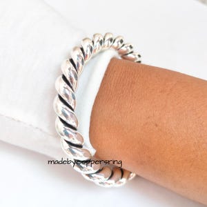 Könnte beinhalten: Ein silberfarbenes Armband mit einem gedrehten Seildesign. Das Armband wird an einem Arm getragen, mit einem weißen Hemdärmel im Hintergrund. Der Text "madebycoppersring" ist unten im Bild zu sehen.