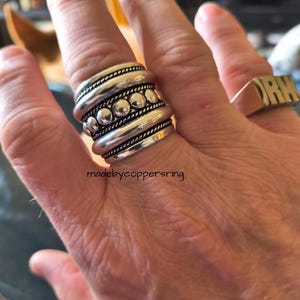 Könnte beinhalten: Ein silberfarbener Ring mit einem geschichteten Design. Der Ring hat mehrere Bänder mit Perlen- und Seiltexturen. Der Text "madebycoppersring" ist unten sichtbar. Ein weiterer goldener Ring mit den Buchstaben "ORM" ist ebenfalls sichtbar.