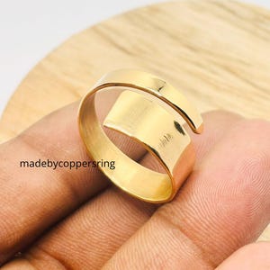 Könnte beinhalten: Ein goldfarbener, verstellbarer Ring mit Wickeldesign. Der Ring wird auf einer Hand gezeigt und trägt den Text "madebycoppersring" an der Seite. Der Ring ist ein schlichtes, elegantes Schmuckstück.