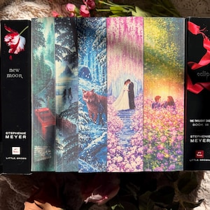 May include: A collection of books featuring custom fore-edge painting on the page edges, displaying a continuous landscape scene with a forest, a wolf, a couple in a wedding setting, and a field of flowers, flanked by two black book spines.