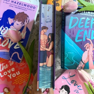 May include: A book with a fore-edge painting on the page edges featuring a couple standing in water, surrounded by other books by Ali Hazelwood. The spine of the central book shows a man and a woman embracing in a pool, with small icons of a medal, a water bottle, and goggles printed above them.