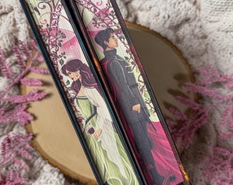 May include: Two hardcover books with illustrated covers. One features a woman in a green dress holding a glass of wine, the other a man in a dark coat and red cape. The spines are black with decorative floral and vine designs.
