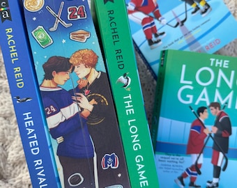 Könnte beinhalten: Eine Sammlung von Büchern von Rachel Reid mit Hockey-Themen auf den Buchcovern. Die Titel lauten unter anderem "Heated Rivalry" und "The Long Game". Die Cover zeigen Illustrationen von Eishockeyspielern in Aktion, mit Fokus auf den Wettbewerbsgeist des Sports.