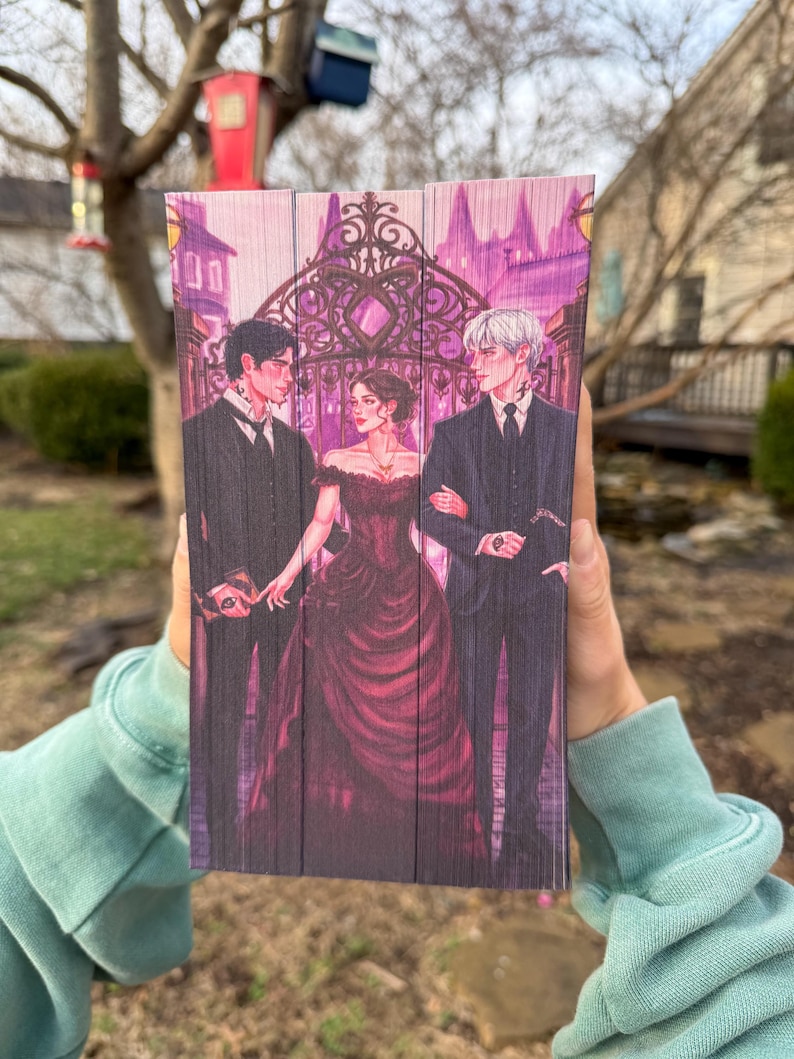 Op de afbeelding: Een houten boek met een fantasie-illustratie. Het kunstwerk toont drie figuren in formele kleding voor een smeedijzeren poort. Het kleurenpalet omvat tinten paars, zwart en rood.