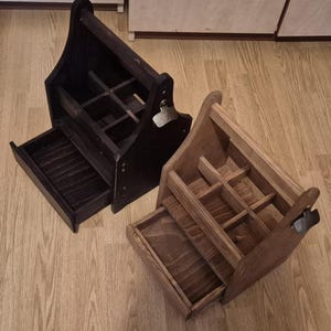 Può includere: Due portabottiglie in legno, uno marrone scuro e l'altro marrone chiaro, su una superficie effetto legno. Ognuno ha un manico, scomparti, un cassetto estraibile e un apribottiglie. I portabottiglie sono progettati per bottiglie.