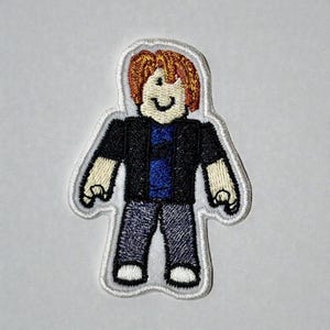 Könnte beinhalten: Gestickter Aufnäher mit einer Zeichentrickfigur mit orangefarbenem Haar, einer schwarzen Jacke, einem blauen Hemd und einer blauen Jeans. Der Aufnäher hat einen weißen Rand und ist zum Aufbügeln oder Aufnähen auf Stoff bestimmt.