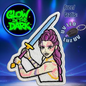 Puede incluir: Parche bordado con una guerrera de pelo morado sosteniendo una espada. El parche tiene un borde blanco y el texto "Glow in the Dark" en verde. También se muestra un pequeño llavero LED UV.
