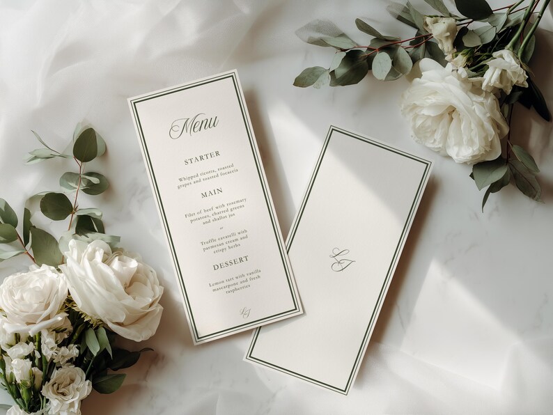 May include: Two ivory-colored menu cards with a dark green border and elegant script. One card displays a menu with headings for Starter, Main, and Dessert. The other card has initials. White roses and greenery are arranged around the cards.