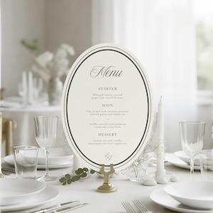Pu&ograve; includere: Un menu ovale con sfondo color crema e bordo nero, che riporta il testo Menu, Starter, Main e Dessert. La carta &egrave; tenuta in posizione verticale da un supporto in metallo dorato su una tavola apparecchiata con piatti bianchi, bicchieri e candele.