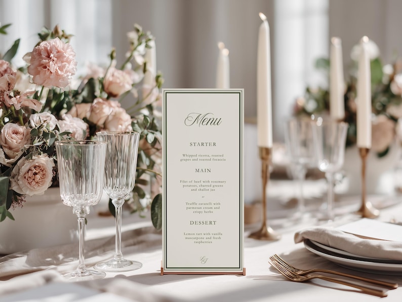 May include: Elegant table setting with a menu card, floral arrangement, and candles. The menu card features a cream background with black text. Two crystal wine glasses are in the foreground. The table is set with plates, silverware, and a linen napkin.