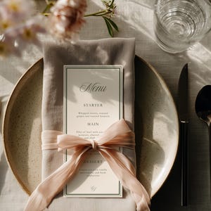 May include: A formal table setting with a menu card, napkin, and silverware. The menu card is cream-colored with black text and a decorative border. A pink ribbon is tied around the napkin. A fork, knife, and spoon are arranged on the table.