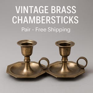May include: A pair of vintage brass chambersticks. Each candlestick features a circular candle cup, a hexagonal base, and a small handle. The image includes the text "VINTAGE BRASS CHAMBERSTICKS".