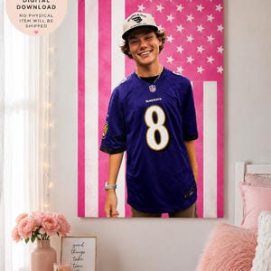 May include: A digital wall art print featuring a person wearing a purple Baltimore Ravens jersey with the number 8 and a white baseball cap, set against a background of a pink and white American flag pattern with stars and vertical stripes.