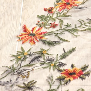May include: Close-up of embroidered floral fabric. The design features vibrant red, yellow, and orange flowers with green leaves and stems. The embroidery is on a sheer, off-white background, creating a delicate and detailed pattern. The fabric is likely used for apparel or home decor.
