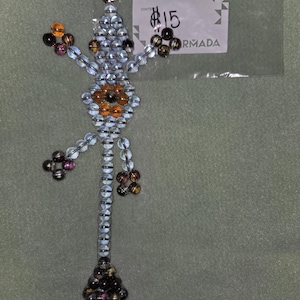 May include: A beaded lizard keyring with a silver ring. The lizard is crafted from clear and iridescent beads, featuring orange and black details. The lizard's body is elongated, and its legs and tail are detailed with clusters of beads.