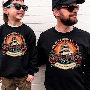 May include: Black sweatshirts featuring a vintage-style sailing ship design within a circular emblem. The emblem includes a rising sun, roses, and the text "EVEN THE WIND AND WAVES OBEY HIM MARK 4:41".