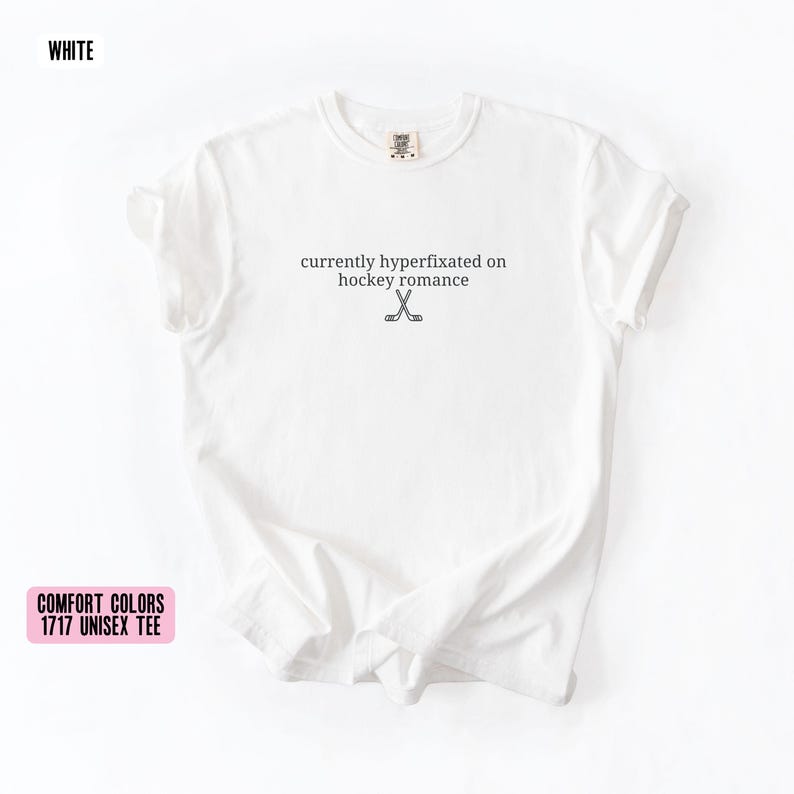 May include: A white short-sleeve t-shirt featuring the black text currently hyperfixated on hockey romance centered on the chest, accompanied by a small graphic of two crossed hockey sticks positioned directly below the printed text.