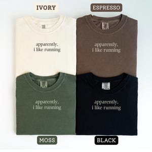 Może przedstawiać: Cztery koszulki w kolorach kości słoniowej, espresso, mchu i czarnym. Każda koszulka ma napis "apparently, i like running" prostą czcionką. Koszulki są złożone i ułożone w kwadrat.