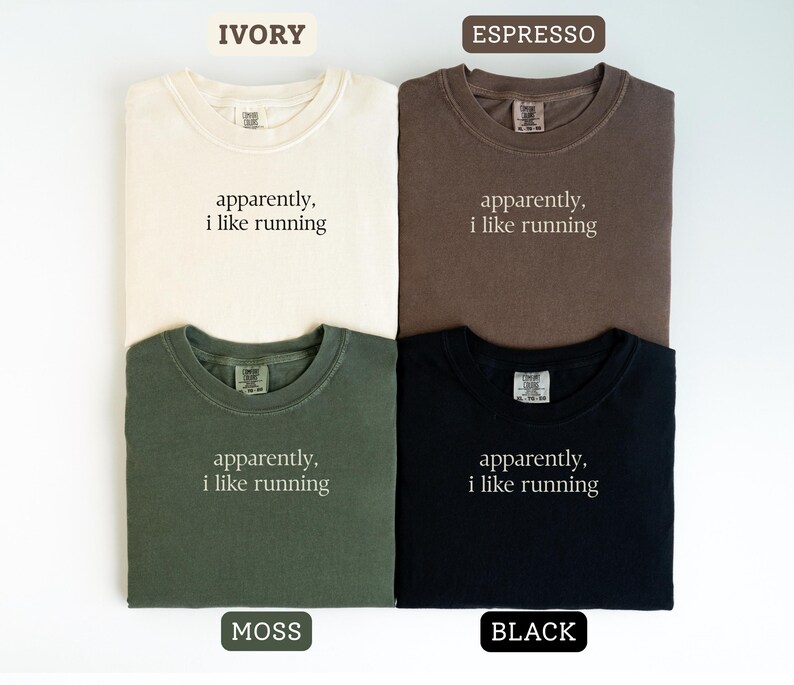 Może przedstawiać: Cztery koszulki w kolorach kości słoniowej, espresso, mchu i czarnym. Każda koszulka ma napis "apparently, i like running" prostą czcionką. Koszulki są złożone i ułożone w kwadrat.