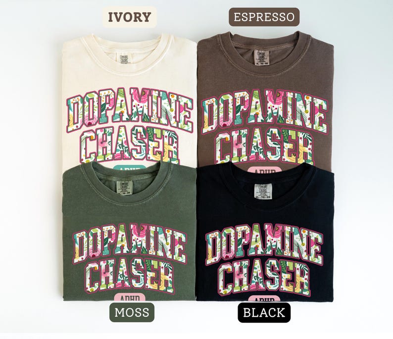 Pode incluir: Quatro camisetas nas cores marfim, caf&eacute;, musgo e preto. Cada camisa apresenta o texto "DOPAMINE CHASER" em um design floral. Gola redonda.