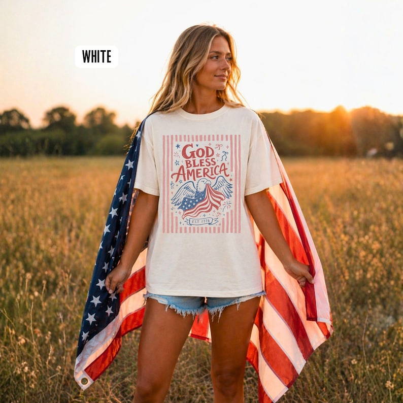 May include: A white t-shirt with a patriotic design featuring an eagle, American flag, and the text "God Bless America." The shirt has a vintage look with red and blue accents and vertical stripes. The word "WHITE" is in the top left corner.
