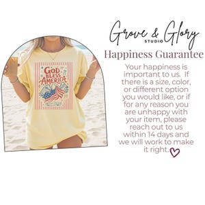 May include: A light yellow t-shirt featuring a patriotic design with an eagle, American flag, and the text "God Bless America." The design is framed by vertical red stripes. The shirt is worn by a person on a beach.