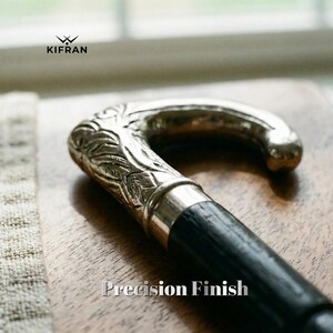 May include: A close-up of a walking cane with a silver-colored, ornate handle and a black wooden shaft. The handle features detailed leaf-like carvings. The text "Precision Finish" is displayed at the bottom of the image. The brand logo "KIFRAN" is at the top left.