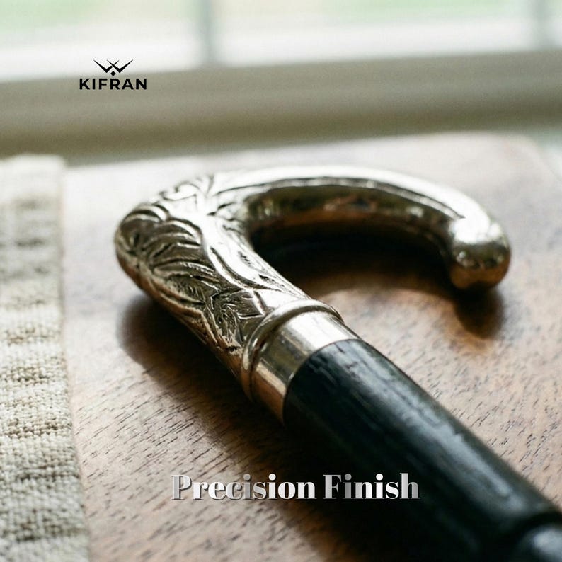 May include: A close-up of a walking cane with a silver-colored, ornate handle and a black wooden shaft. The handle features detailed leaf-like carvings. The text "Precision Finish" is displayed at the bottom of the image. The brand logo "KIFRAN" is at the top left.