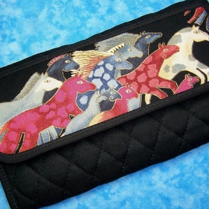 May include: Black quilted clutch with a flap featuring a colorful horse design. The horses are in shades of red, pink, blue, and white. The clutch is a rectangular shape with a curved flap.