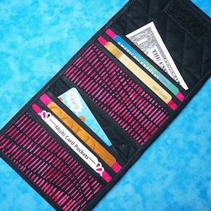 May include: Black quilted wallet with pink and black patterned fabric. The wallet is open and has multiple card slots and a cash pocket. The wallet contains credit cards, a gift card, and a dollar bill.