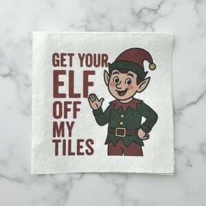 May include: White square with the text "GET YOUR ELF OFF MY TILES" in maroon. A cartoon elf with green clothing, a maroon hat, and pointy ears is waving. The elf has a smiling expression.