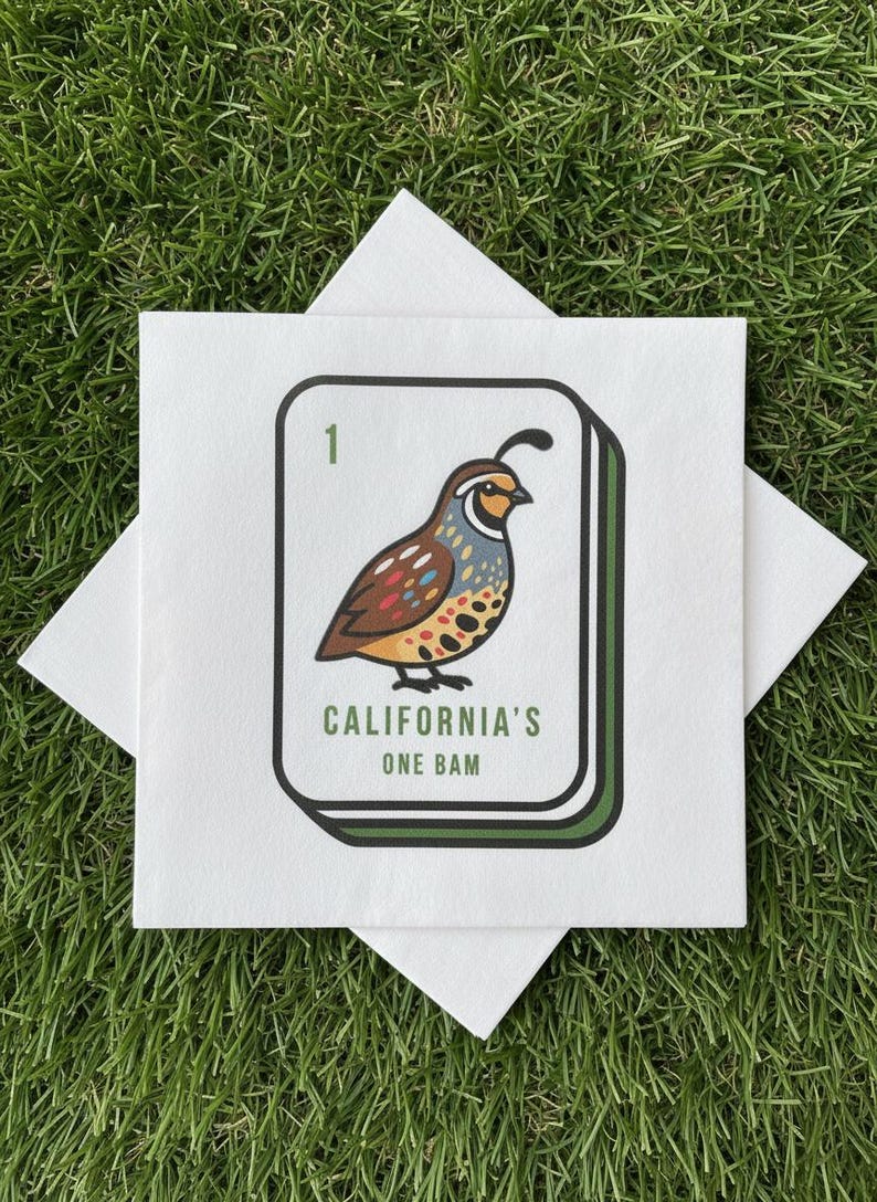 May include: White square napkin featuring a quail bird illustration, with text reading "CALIFORNIA'S ONE BAM". The bird is depicted in brown, tan, and blue. The napkin rests on green grass.