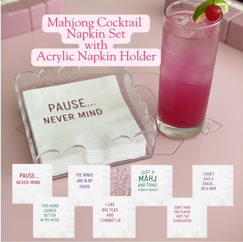 May include: A Mahjong Cocktail Napkin Set with an acrylic napkin holder. The set includes white napkins with phrases like "PAUSE... NEVER MIND" and "JUST A MAHJ AND TONIC KIND OF NIGHT". A pink cocktail with a cherry garnish is also in the image.