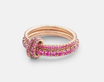 Può includere: Un anello in oro rosa caratterizzato da un design a fascia continua, impreziosito da numerose piccole pietre preziose rosa brillante incastonate lungo l'intera circonferenza, con un dettaglio a nodo circolare anch'esso tempestato di pietre.