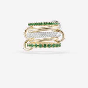 May include: A stack of gold rings interlocked with a silver ring. Two rings are adorned with green gemstones, one with white gemstones, and two are plain gold. The rings are displayed against a white background.
