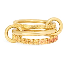 May include: Three gold-coloured rings interlocked. Two rings are embellished with small, yellow and orange gemstones, while the central ring is a solid band. The rings are designed to be worn together.