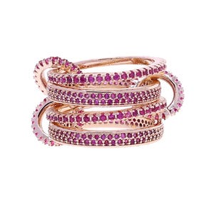 May include: A stack of rose gold rings with a continuous design. Each ring is encrusted with small, vibrant pink gemstones. The rings are interlocked, creating a unique and eye-catching jewellery piece.