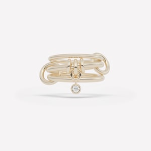 May include: A gold ring with a distinctive design. It features multiple linked loops and a small, dangling diamond. The ring's design is modern and elegant, suitable for everyday wear or special occasions.