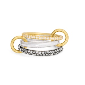 May include: Four interlinked rings. One is gold with small clear stones, another is clear, and the third is black with small clear stones. The fourth ring is gold and connects the other rings.