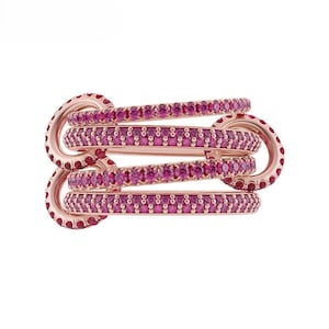 May include: A rose gold ring with multiple bands interlocked. Each band is encrusted with small, vibrant pink gemstones. The ring has a unique, intertwined design, showcasing a modern and elegant aesthetic. The gemstones are evenly spaced, creating a continuous line of color.